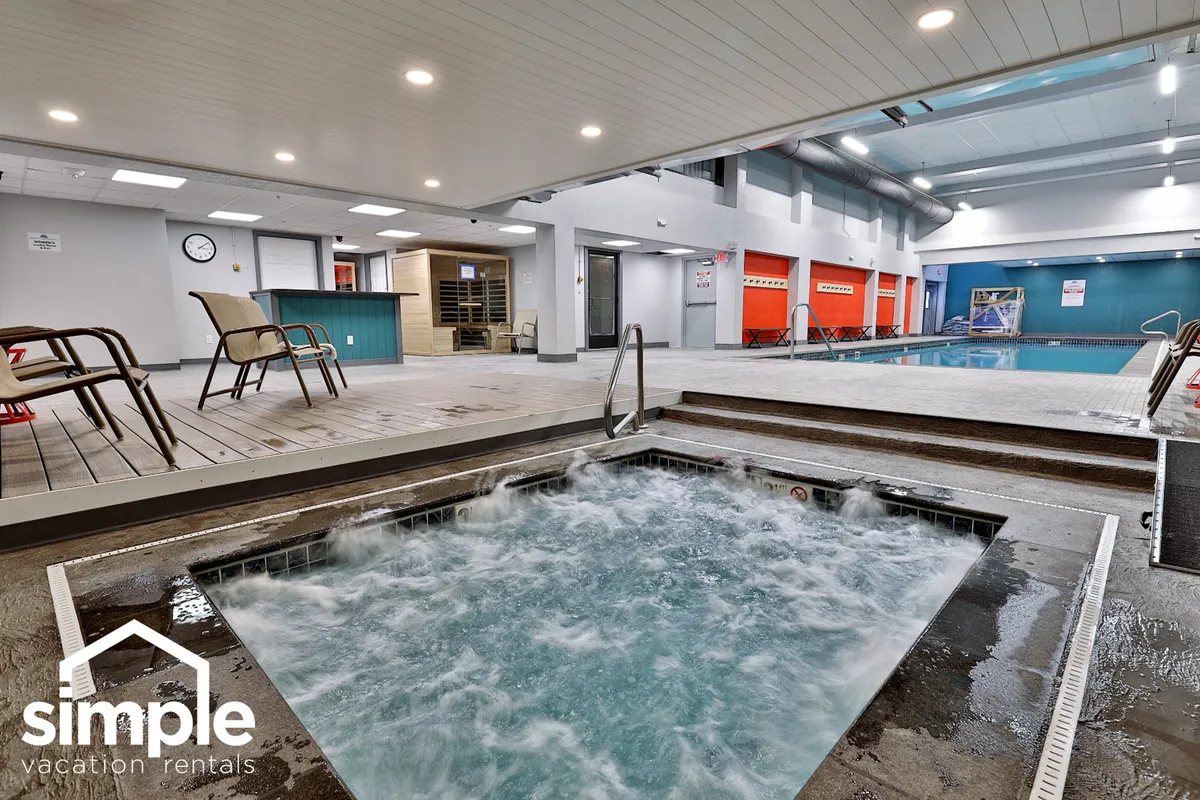 This inviting interior image captures a spacious indoor pool area with a bubbling hot tub and ample poolside seating. The space is bathed in gentle, calming light, encouraging relaxation, swimming, and socializing in a resort-like environment.