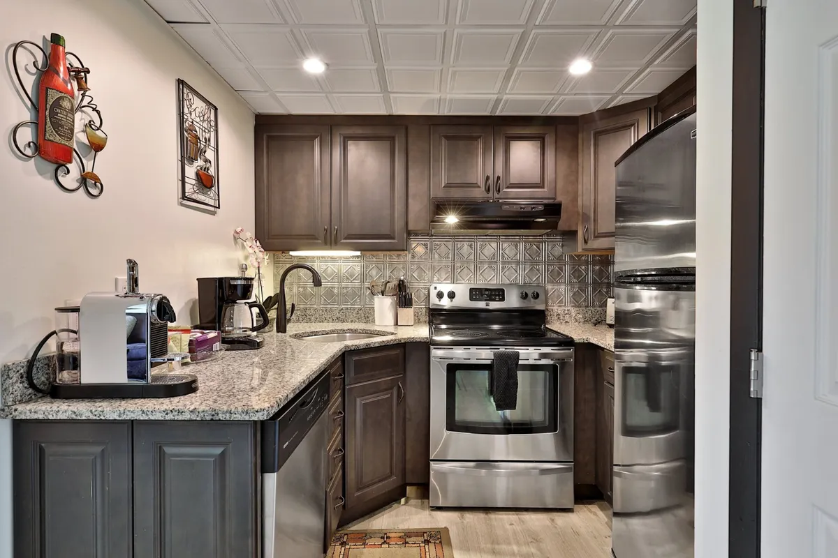 A warm and welcoming kitchen featuring stainless steel appliances, a granite countertop, decorative wall art, and a visible coffee maker. The space suggests activity, with the potential for cooking, entertaining, and coffee brewing, all set in an inviting atmosphere.