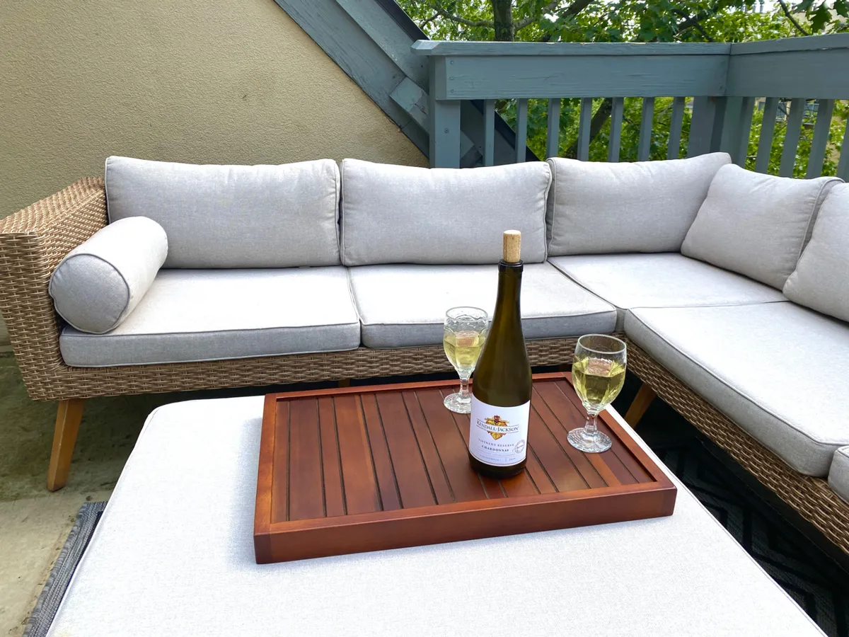 The photo highlights a stylish outdoor sectional sofa with wine glasses and a wine bottle on a wooden tray, set against a backdrop of natural greenery. The space feels inviting and perfect for celebrating special moments or unwinding after a day of exploration.