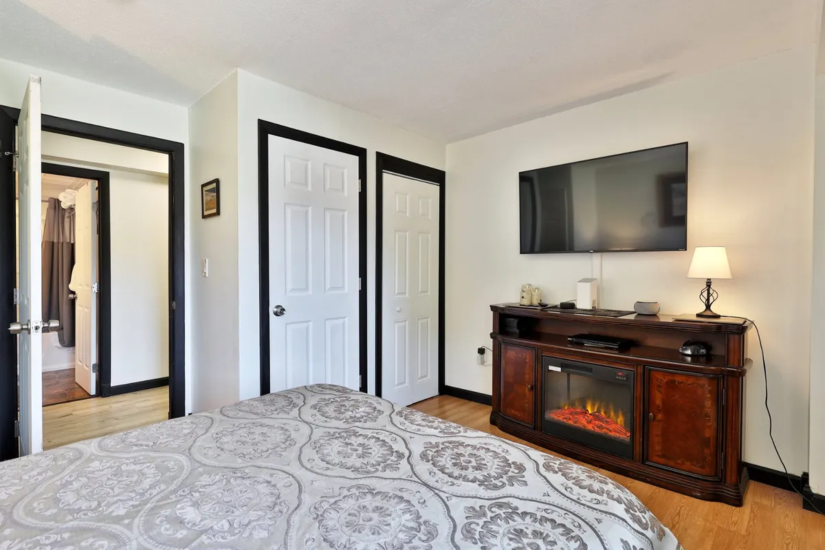 This image features a queen-sized bed adorned with patterned bedding, a television mounted on the wall, and a console table with an electric fireplace beneath the TV. The room exudes a cozy and welcoming ambiance, ideal for relaxation and unwinding after a day of adventure.