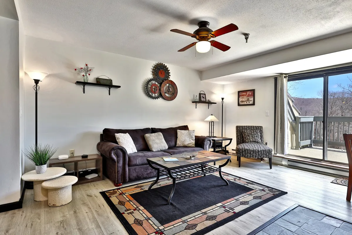 A modern living area showcasing a plush sofa, coffee table, tasteful wall art, and a sliding glass door leading to a balcony. The room is filled with natural light, emphasizing the transition between indoor comfort and outdoor scenery.