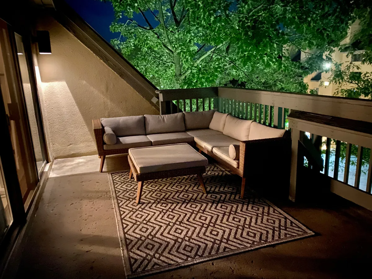 This exterior shot features an intimate outdoor seating area with a sofa, ottoman, textured rug, and lush green surroundings. The mood is serene and private, ideal for stargazing or quiet conversations.
