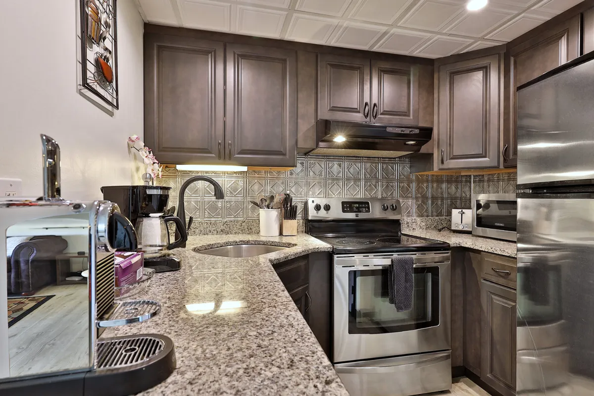 A cozy kitchen scene featuring a granite countertop, stainless steel appliances, decorative backsplash, kitchenware, and a coffee maker. The ambiance suggests a space for cooking, entertaining, and enjoying morning coffee.
