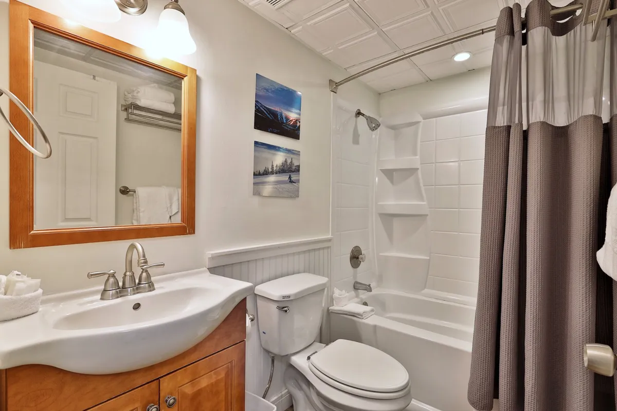 A spotless, modern bathroom with a vanity and sink, large mirror, bathtub, shower curtain, and decorative wall art. The space is inviting and well-equipped for bathing and grooming.